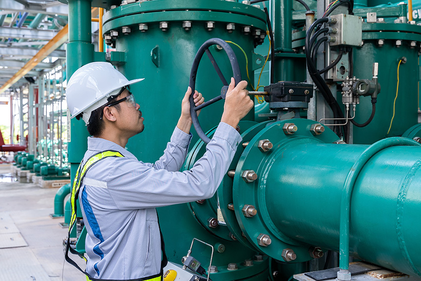 Man wearing hard hat adjusts industrial pipes.