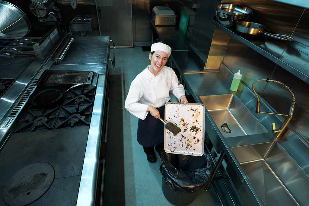 Chef in commercial kitchen holding tray with food scraps