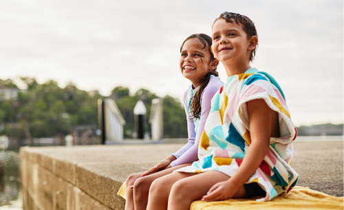 2 children on a suburban wharf, sitting on towels after swimming