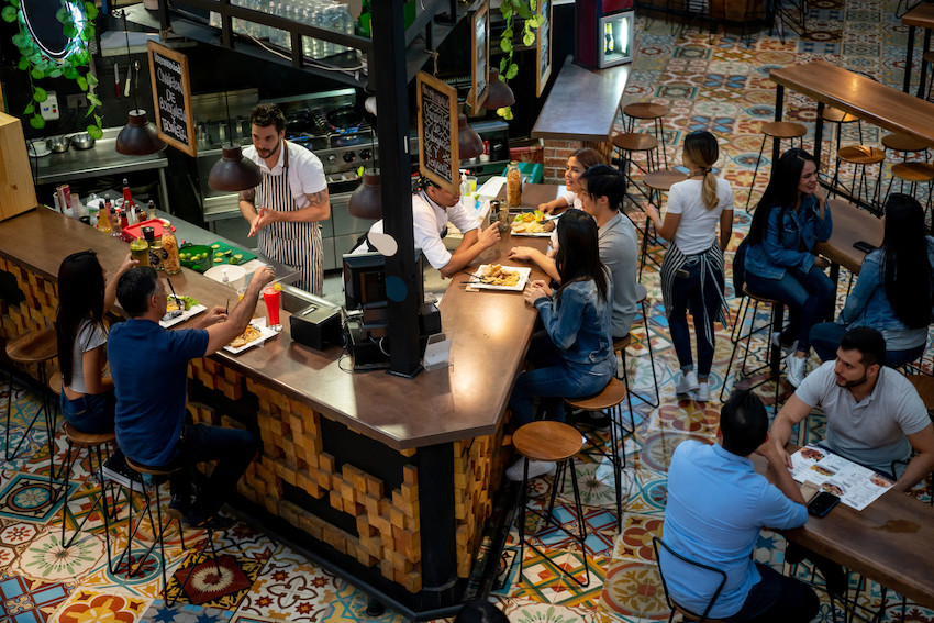 Food court with a central food vendor and surrounding chairs and tables with people enjoying their meals
