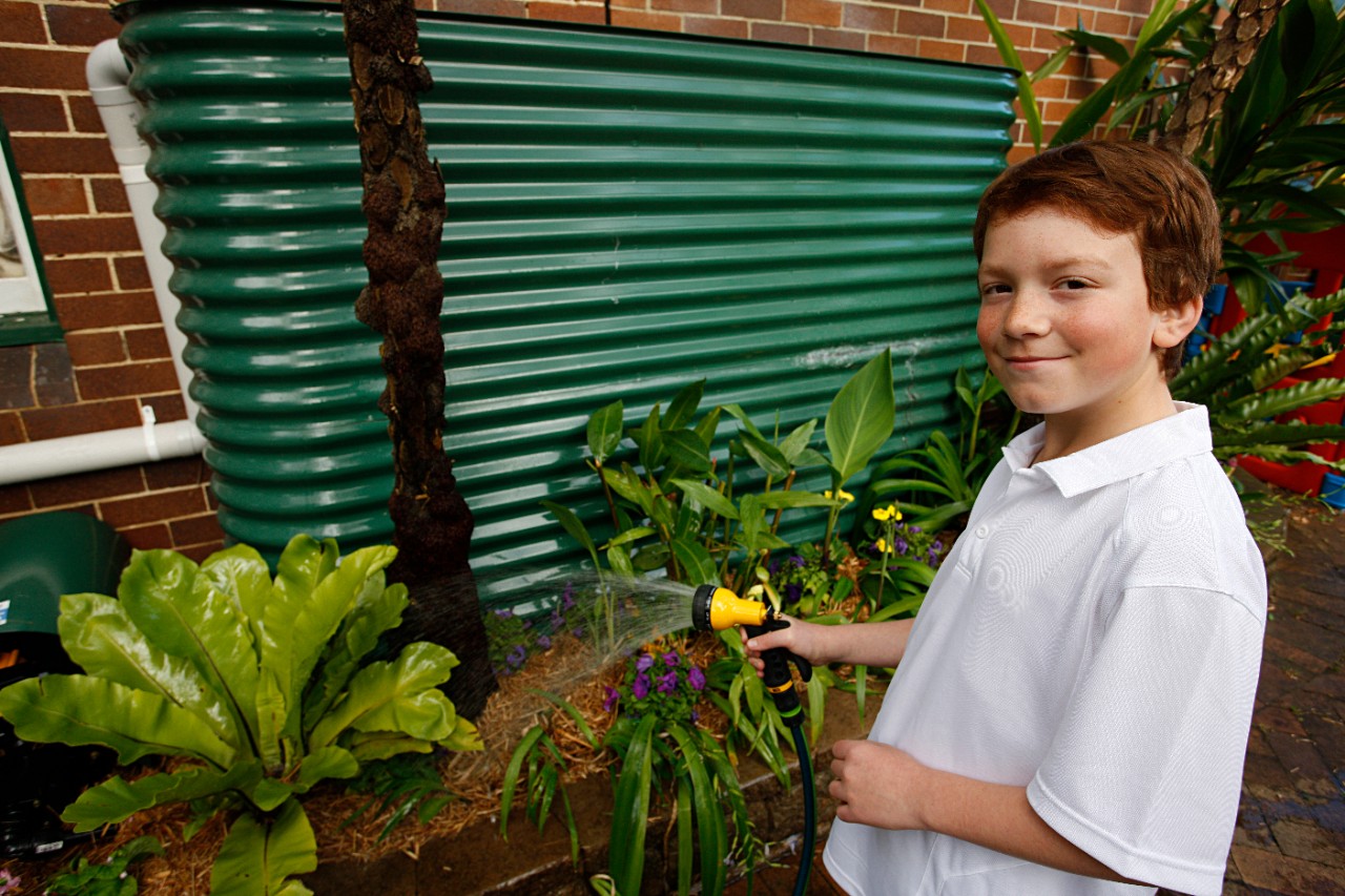 A photo of a boy watering the garden by a rainwater tank.