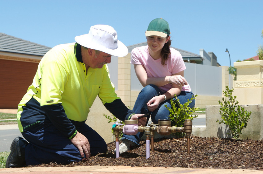 Two people looking at water meters at the front of a property