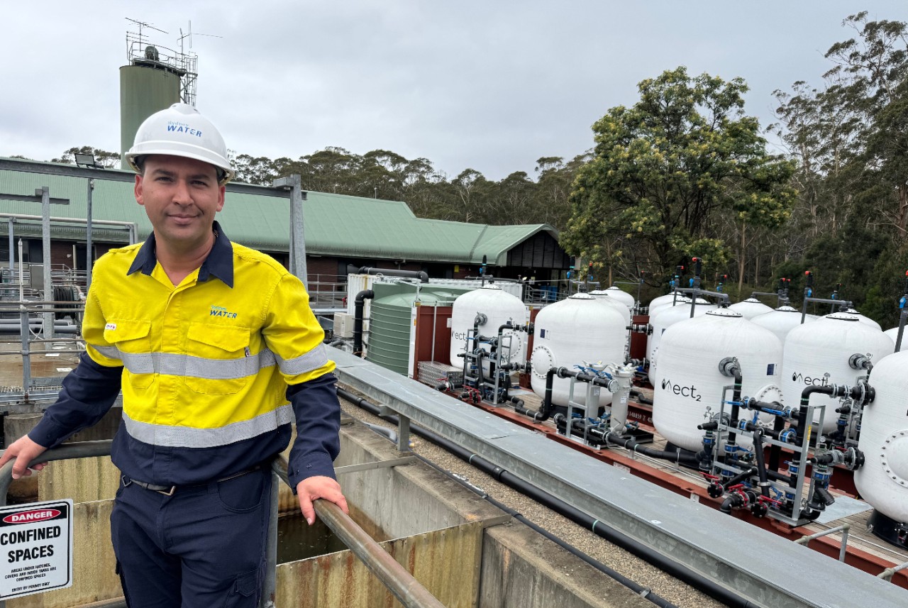 White filtration tanks at Cascade Water Filtration plant connected by pipework and valves with Sydney Water employee. 