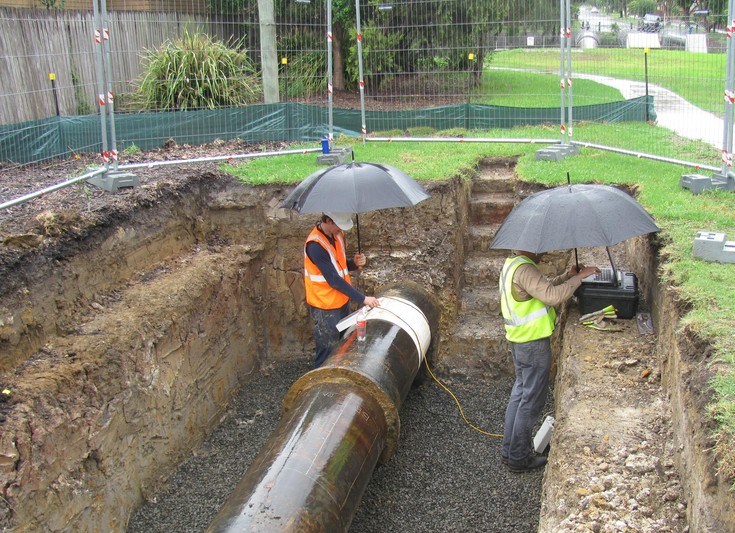 Two Sydney Water staff using a listening device on large pipes