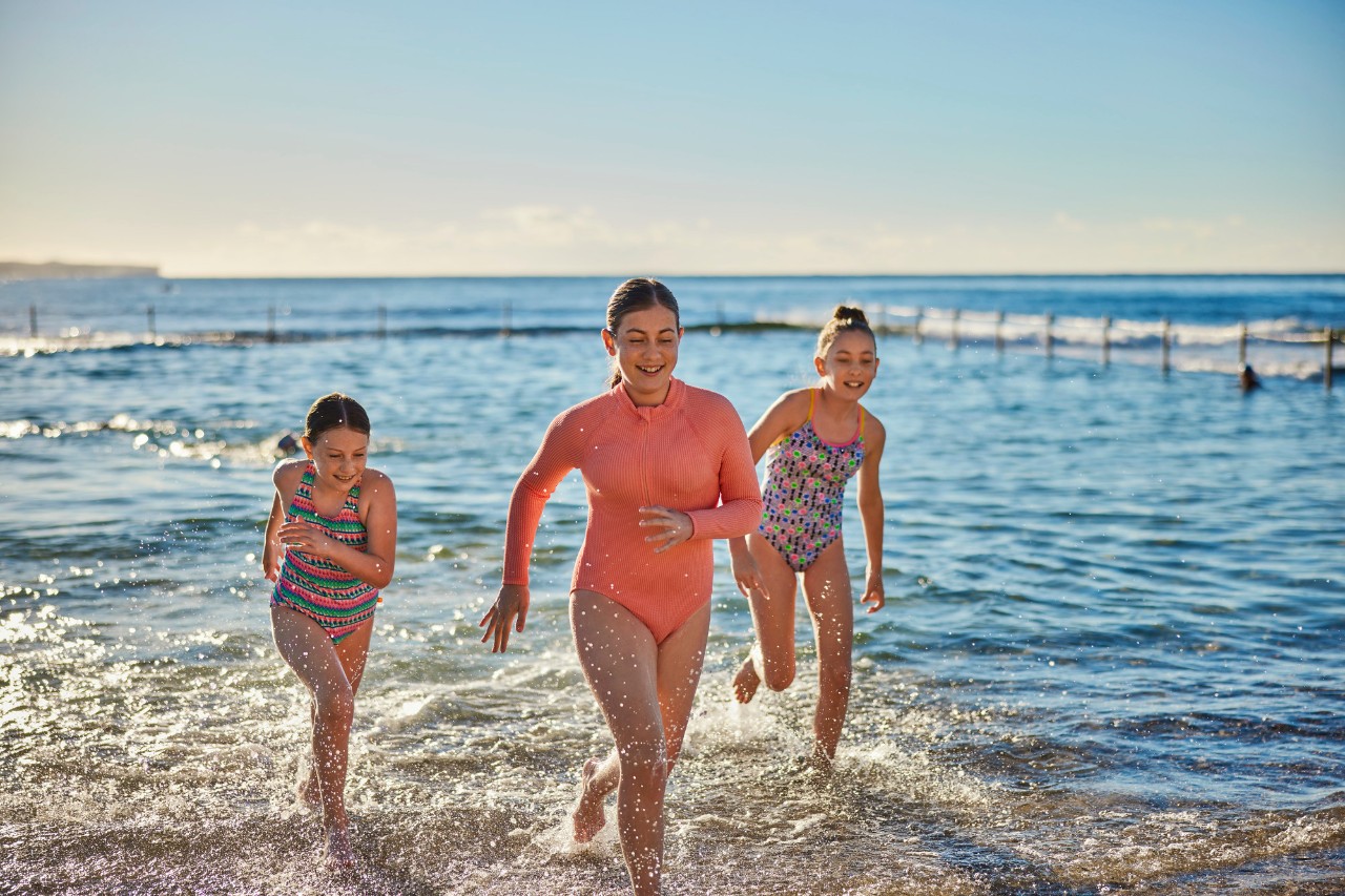 Three girls running out of the water at an ocean swimming pool