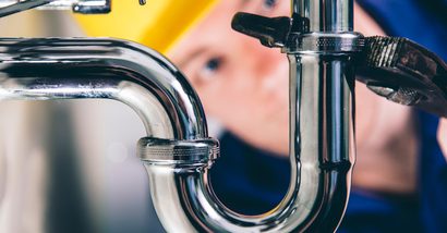 Plumber fixing a drain with adjustable wrench. Focus on drain, plumber defocused in back.