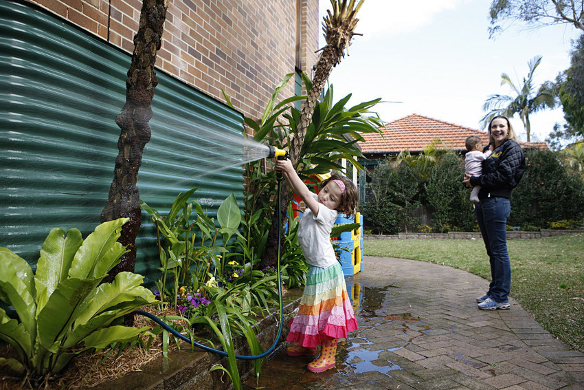 A child watering a garden next to a rainwater tank. 