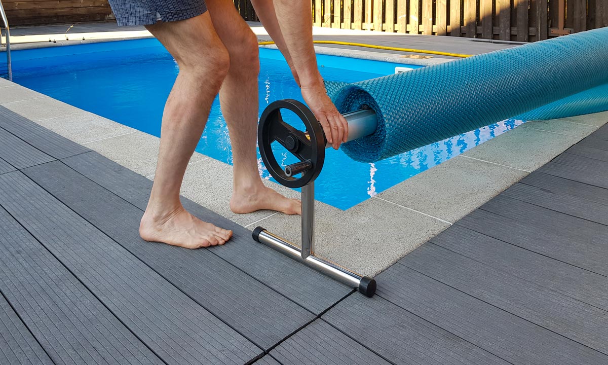 Man spreading a pool blanket using a roller.